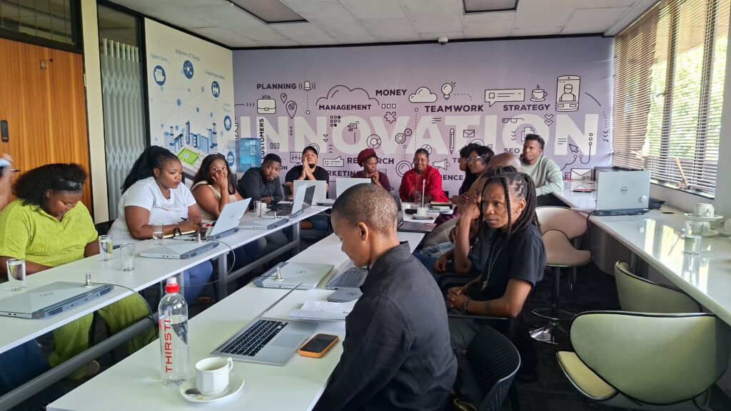 Entrepreneurs working on laptops around a table in front of an innovation-themed wall mural at Softstart BTI